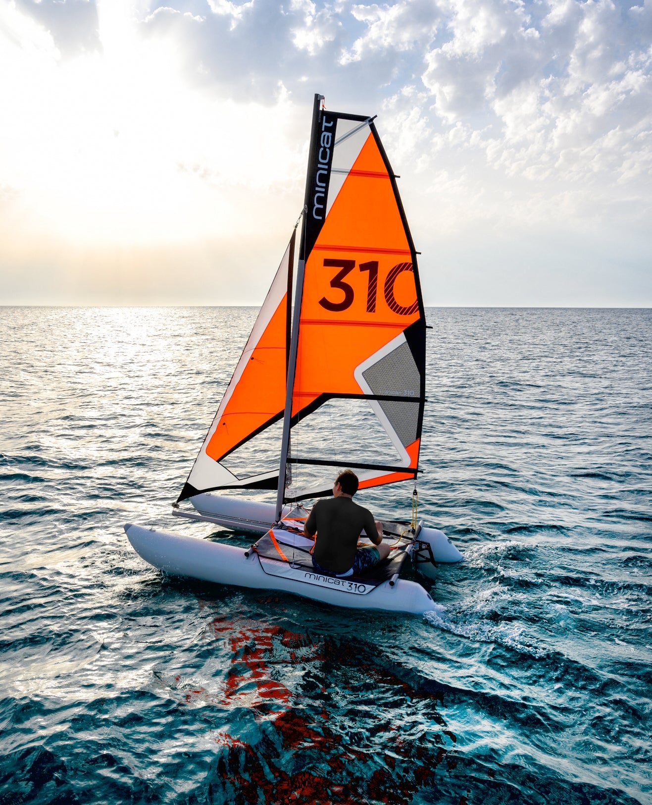 Person sailing on a small boat MiniCat with an orange sail labeled '310' on a calm sea.