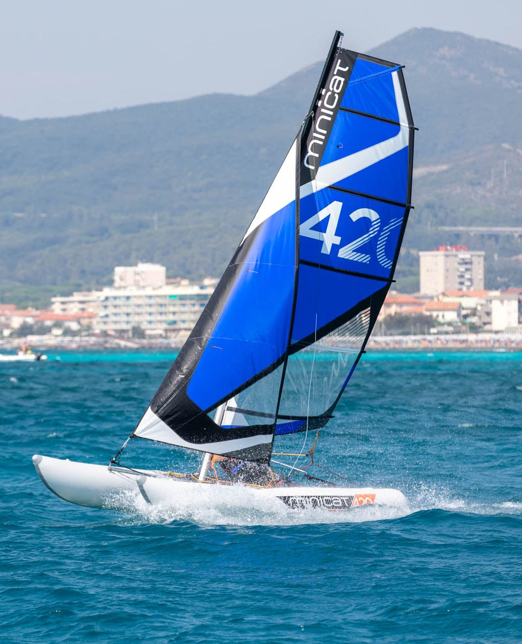 Sailboat MiniCat with a blue and black sail on the water with mountains in the background