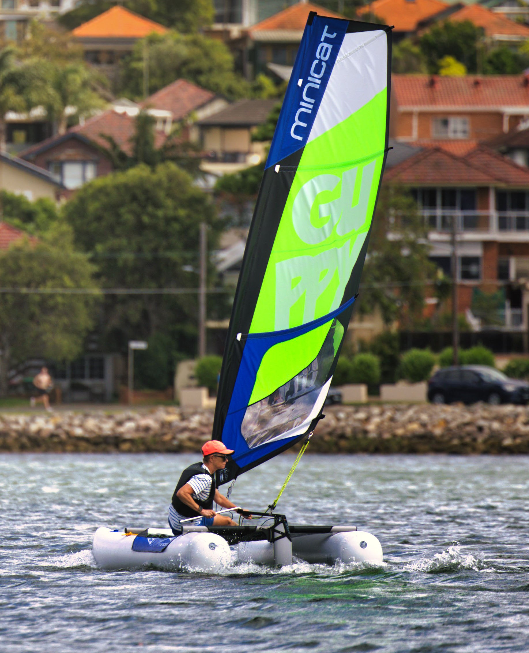 Person sailing MiniCat on the water with residential buildings in the background