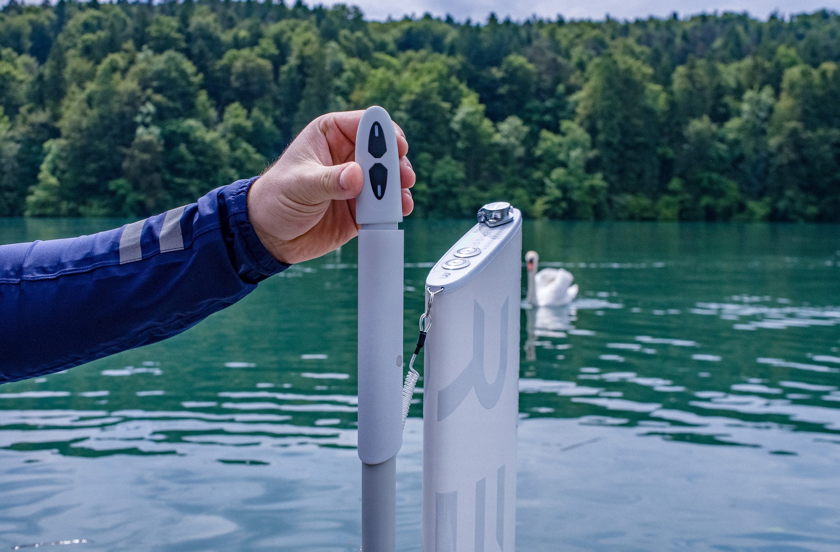 Person holding a device - starting key on a dock with a lake and trees in the background
