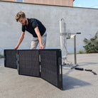 Person setting up a solar panel on a concrete surface with a building in the background